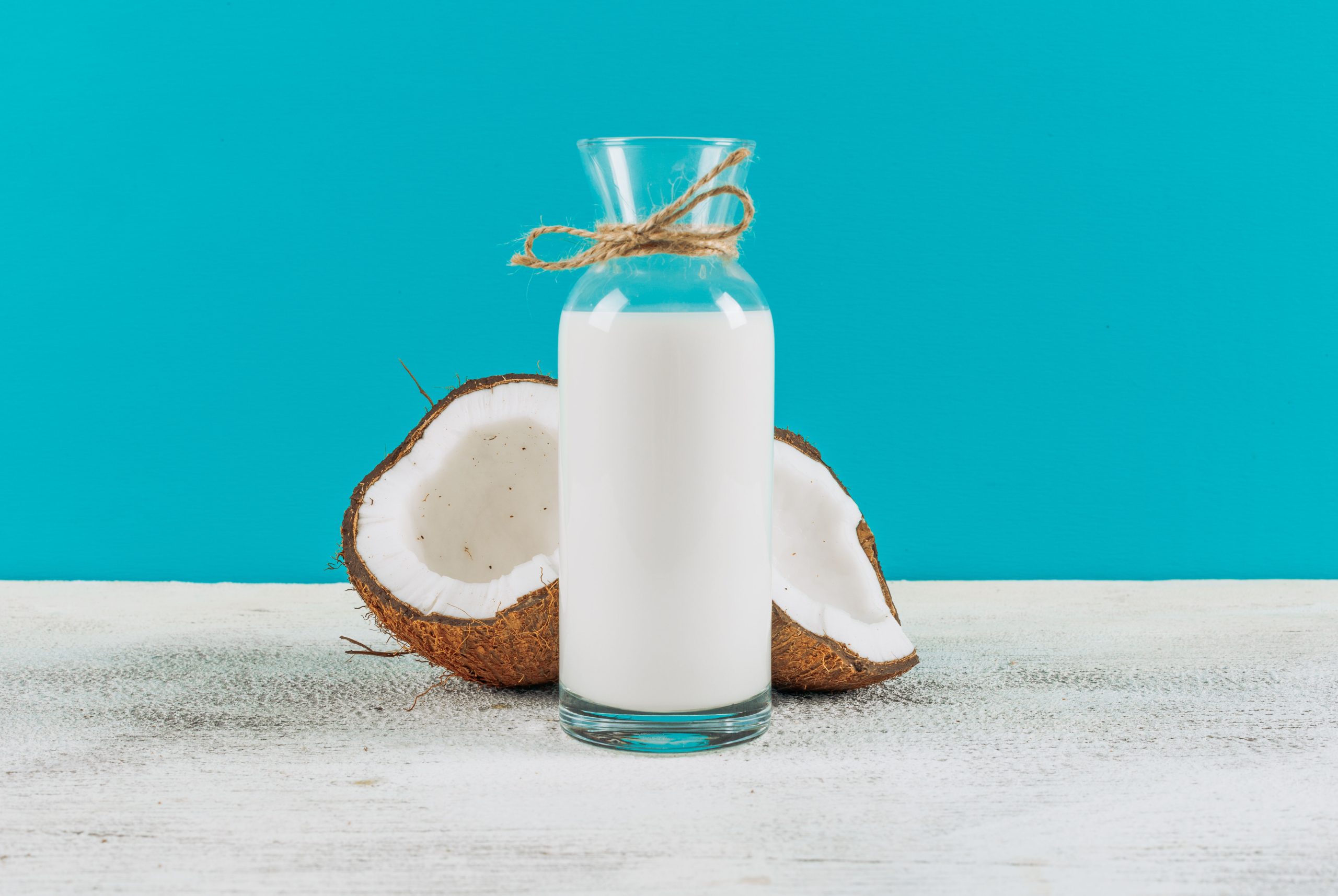 bottle-milk-with-divided-half-coconuts-side-view-white-wooden-background (1)